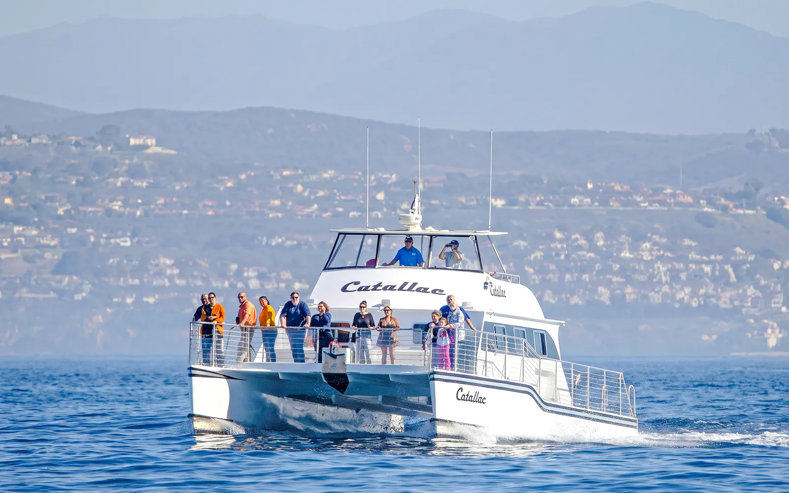 Catamaran with tourists on a whale watching cruise near coastal hills.