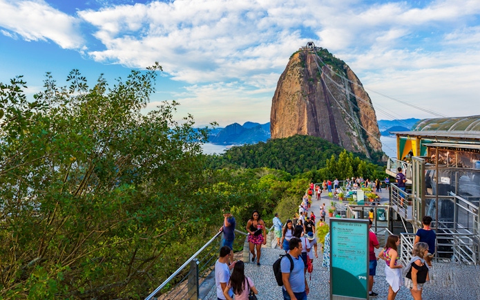 Visitors at Sugarloaf Mountain, Rio de Janeiro, with cable car and scenic views.