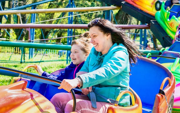 Woman and girl enjoying a colorful amusement park ride.