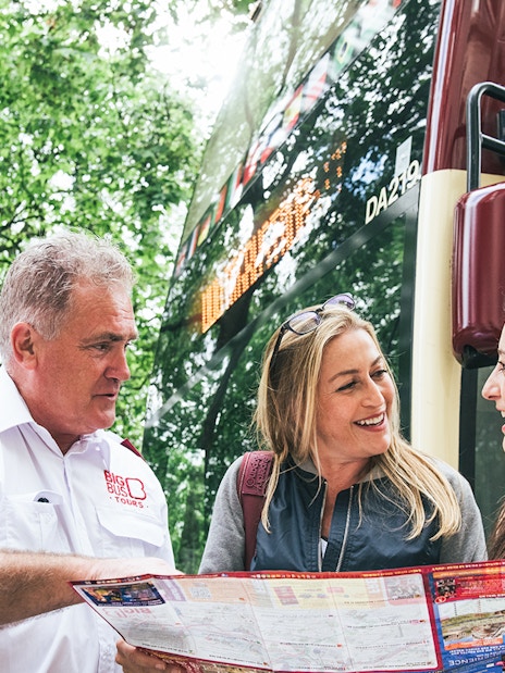 Big Bus employee assisting tourists with a map near a tour bus.