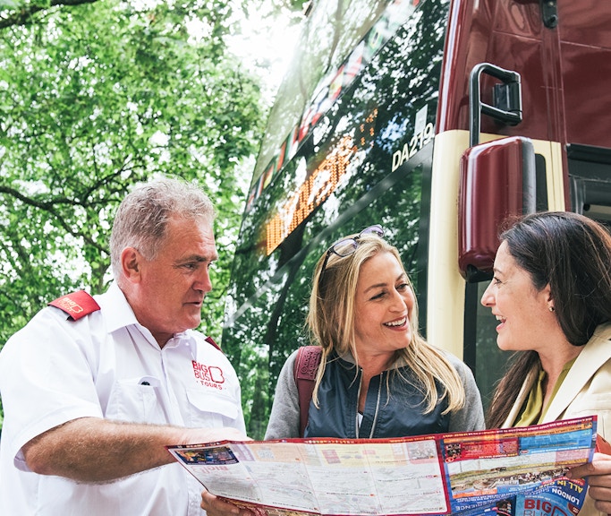 Big Bus employee assisting tourists with a map near a tour bus.