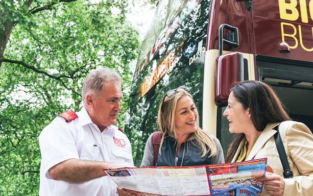 Big Bus employee assisting tourists with a map near a tour bus.