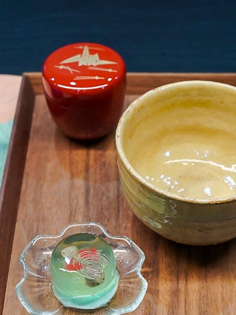 Teapot, matcha bowl, whisk, and sweet on a wooden tray for a tea ceremony.