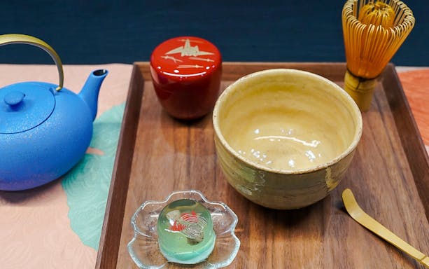 Teapot, matcha bowl, whisk, and sweet on a wooden tray for a tea ceremony.