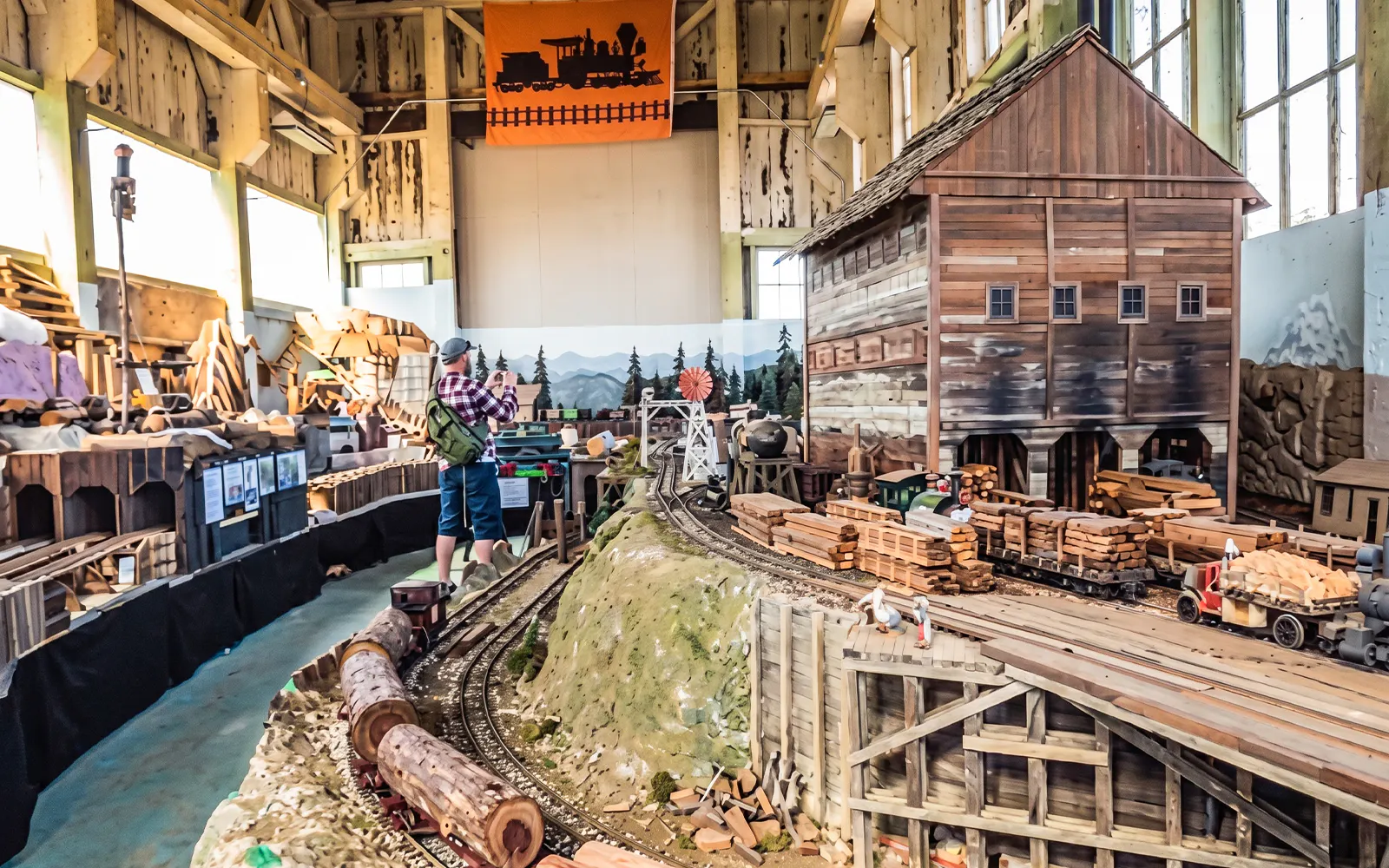 Visitor exploring model train exhibit with detailed railroads and wooden structures.