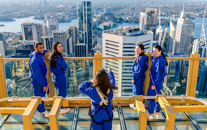 Group on Sydney Tower Eye Skywalk overlooking cityscape and Sydney Harbour Bridge.