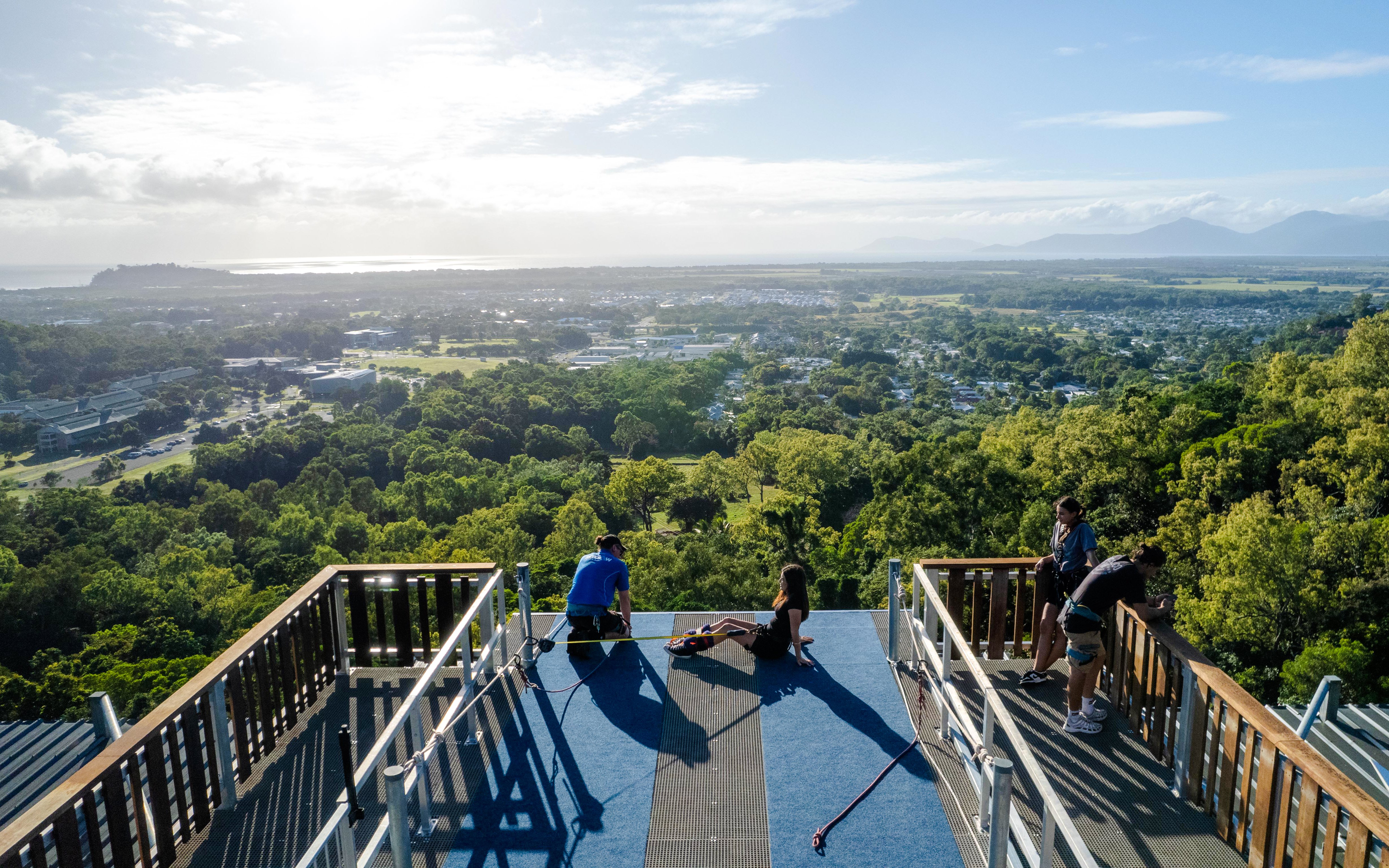 People preparing for Walk The Plank by AJ Hackett, overlooking lush landscape and distant mountains.