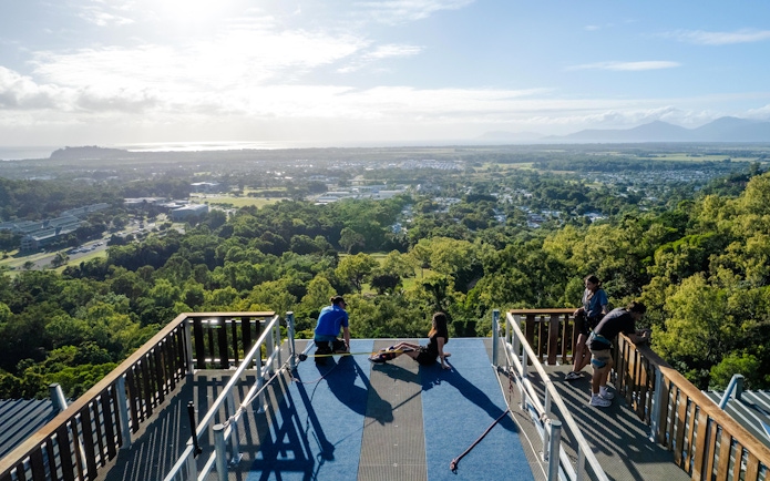People preparing for Walk The Plank by AJ Hackett, overlooking lush landscape and distant mountains.