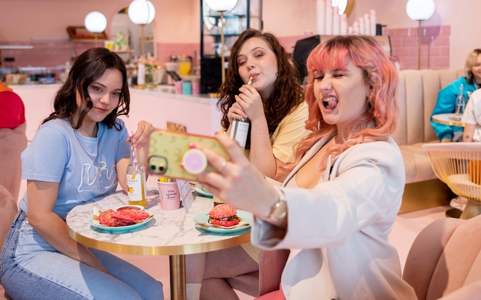 Friends taking a selfie at Upside Down Amsterdam cafe with colorful drinks and snacks.