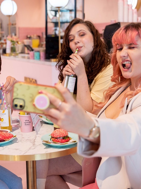 Friends taking a selfie at Upside Down Amsterdam cafe with colorful drinks and snacks.