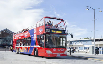 Red double-decker bus on Hobart Hop-On Hop-Off tour with passengers waving.