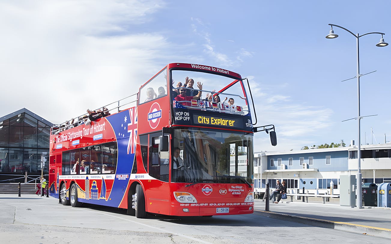 Red double-decker bus on Hobart Hop-On Hop-Off tour with passengers waving.