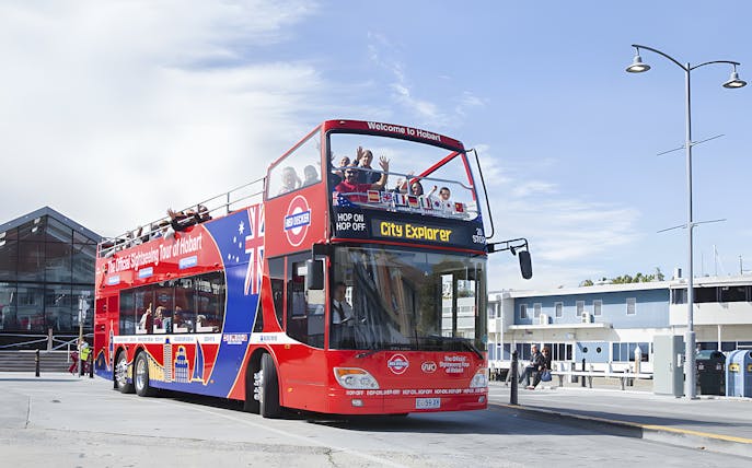 Red double-decker bus on Hobart Hop-On Hop-Off tour with passengers waving.