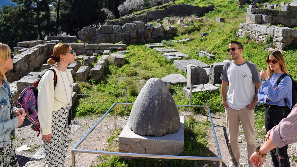Visitors exploring the ancient ruins at Delphi, Greece, near the Omphalos stone.