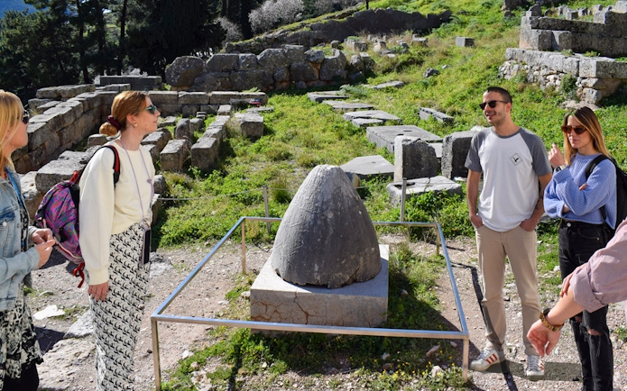 Visitors exploring the ancient ruins at Delphi, Greece, near the Omphalos stone.
