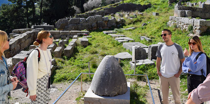 Visitors exploring the ancient ruins at Delphi, Greece, near the Omphalos stone.