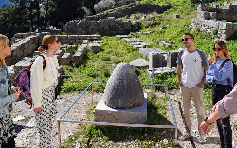 Visitors exploring the ancient ruins at Delphi, Greece, near the Omphalos stone.