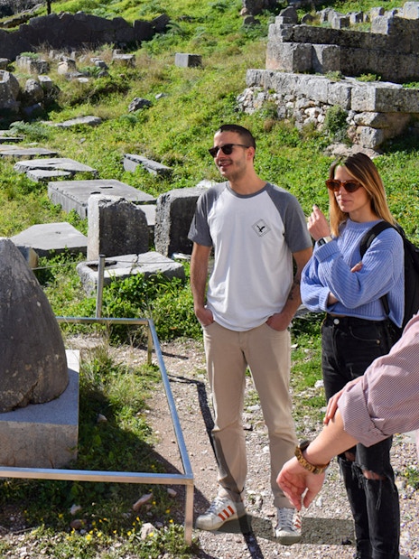 Visitors exploring the ancient ruins at Delphi, Greece, near the Omphalos stone.