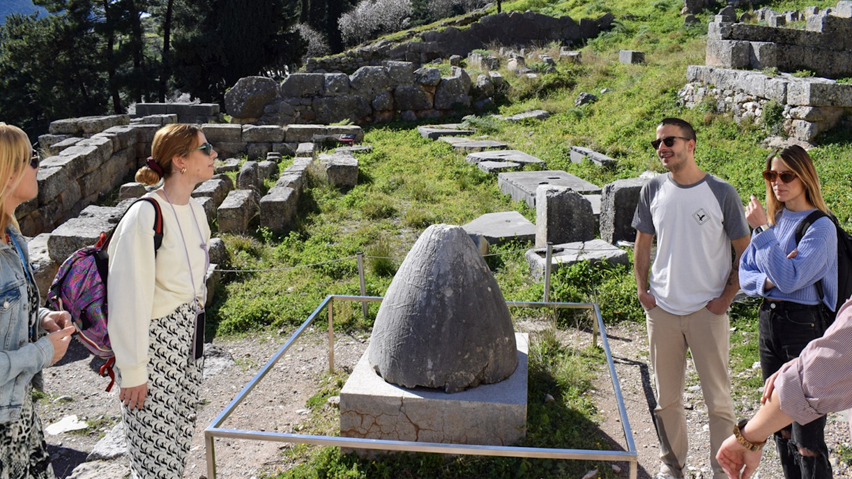 Visitors exploring the ancient ruins at Delphi, Greece, near the Omphalos stone.