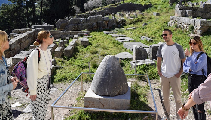 Visitors exploring the ancient ruins at Delphi, Greece, near the Omphalos stone.
