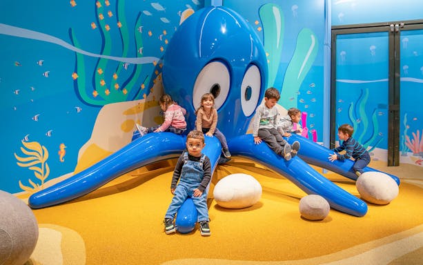 Children playing on a blue octopus sculpture at City of Kids, Genoa.