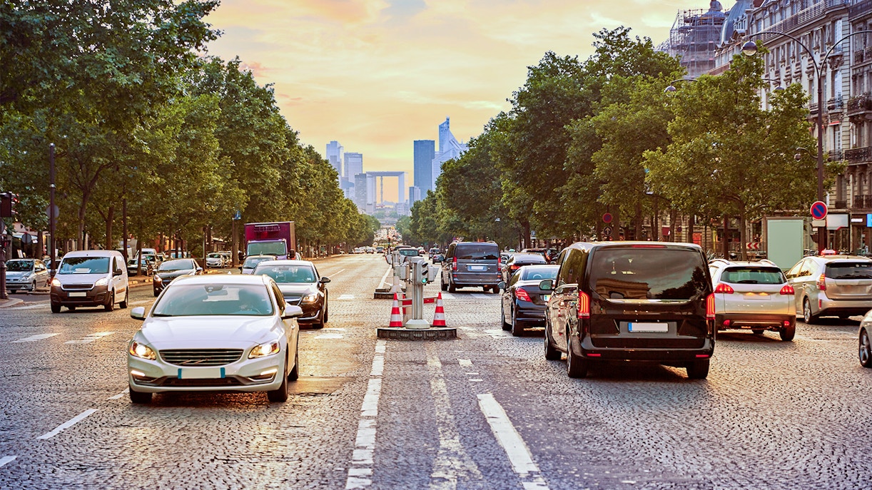 Traffic on a Paris street with La Défense skyline in the distance.