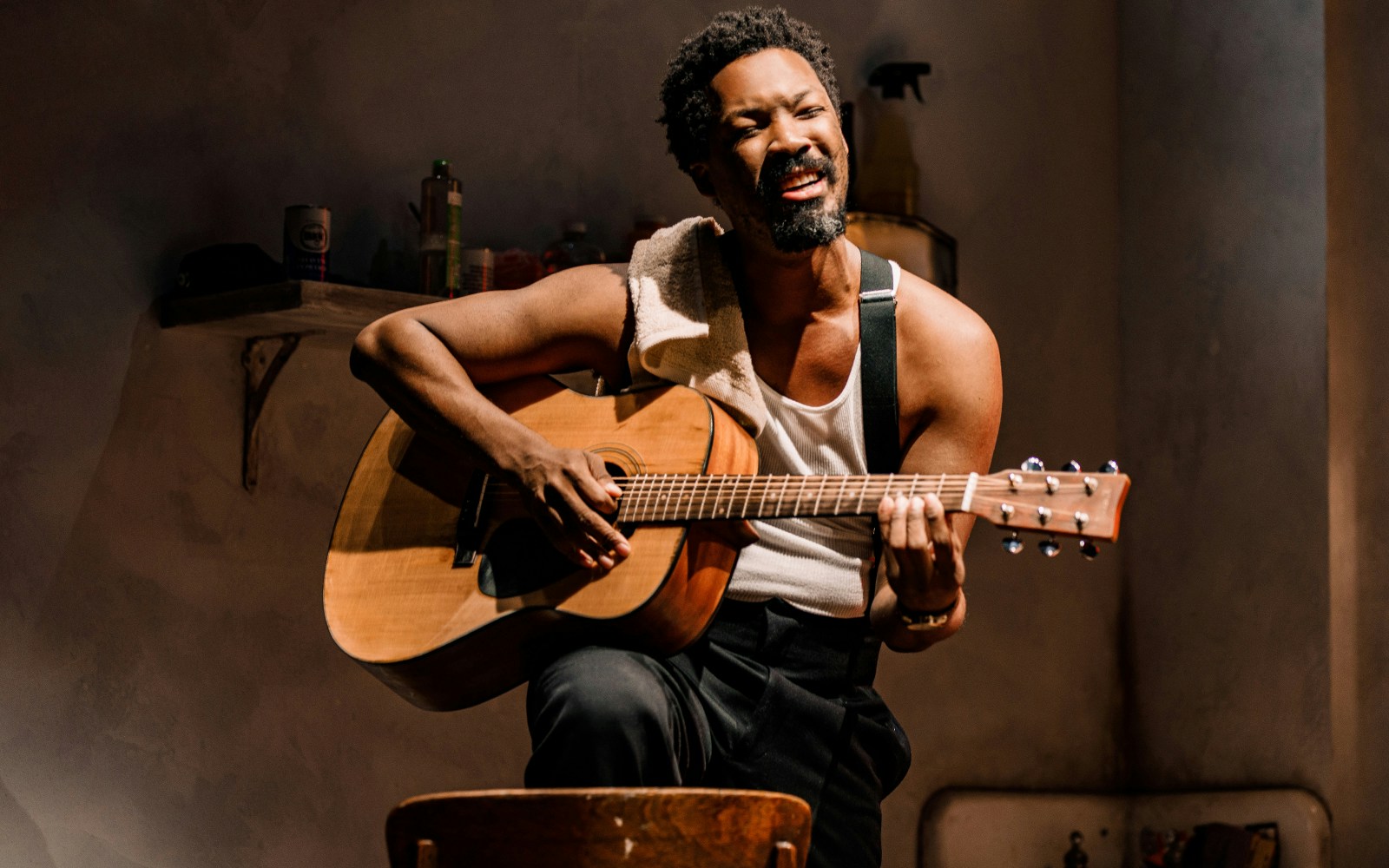 Man playing guitar in a dimly lit room, related to Topdog/Underdog performance.