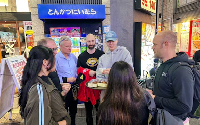Group enjoying street food on Shinjuku food tour in Tokyo, sampling dishes outside an eatery.
