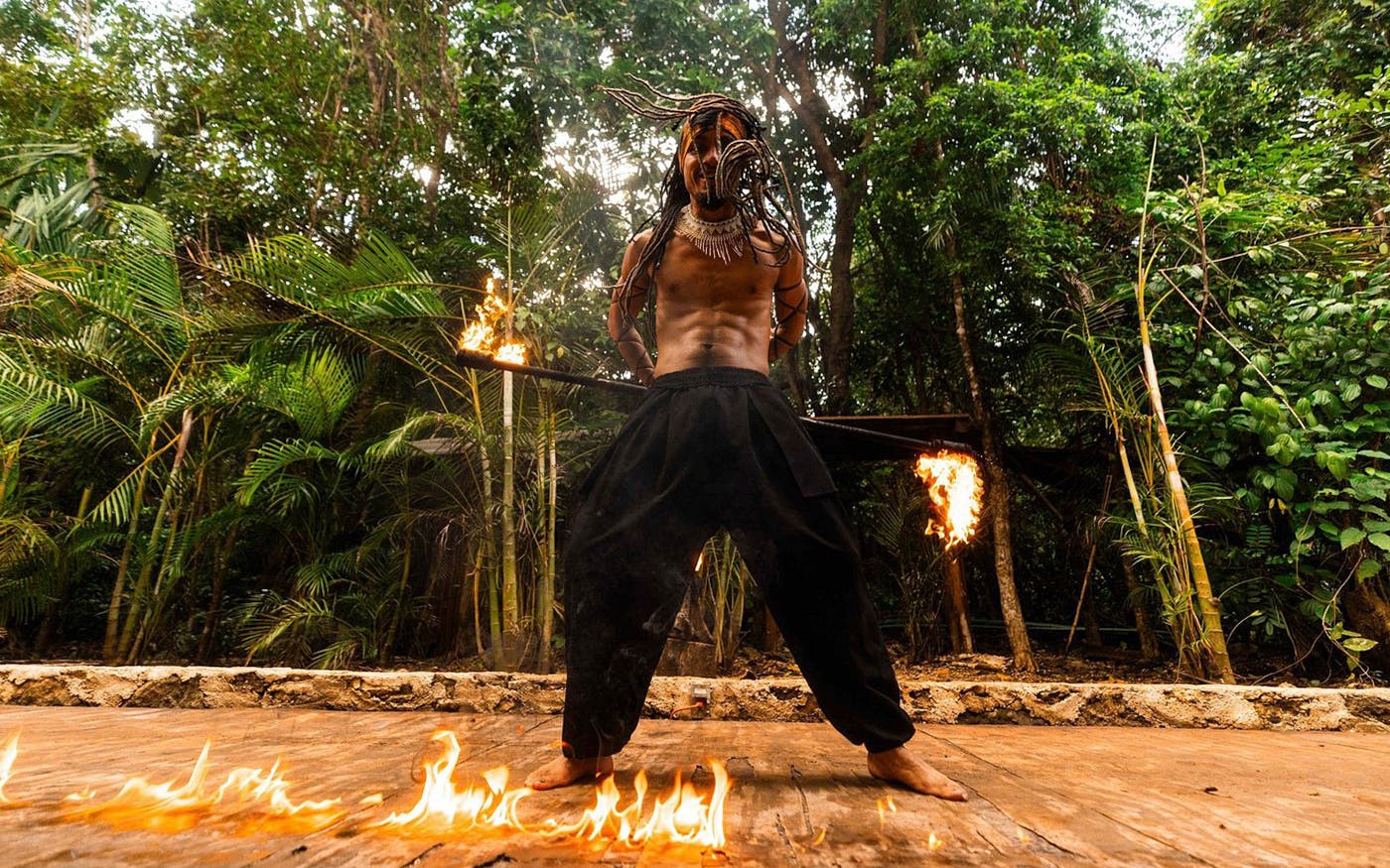 Performer with flaming sticks in Cancun jungle setting.