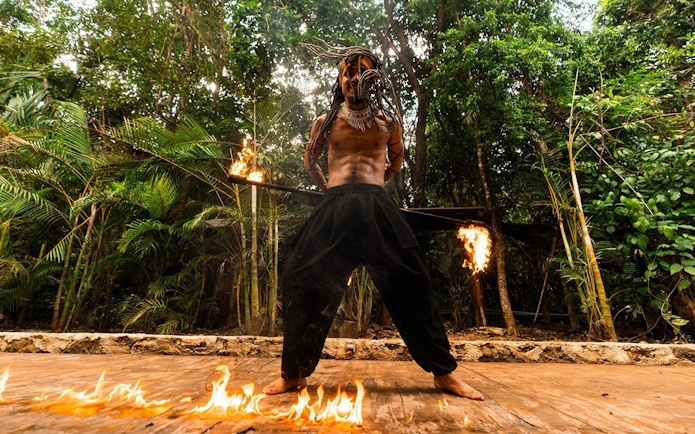 Performer with flaming sticks in Cancun jungle setting.