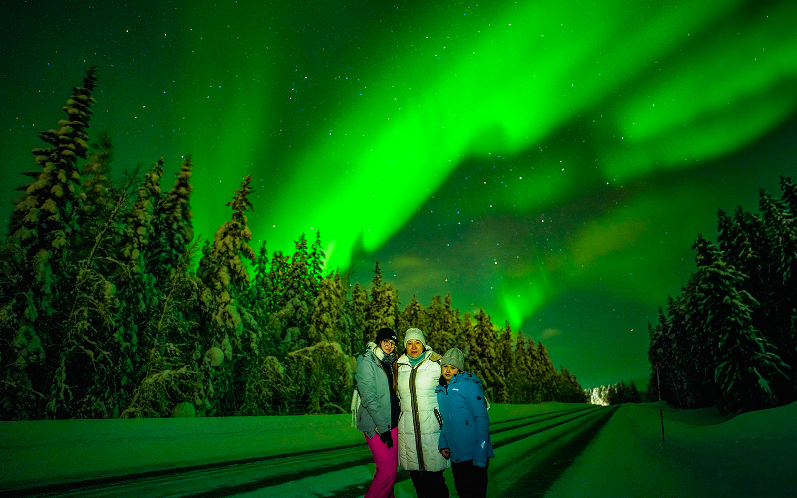 Family enjoying Northern Lights in snowy Rovaniemi forest.