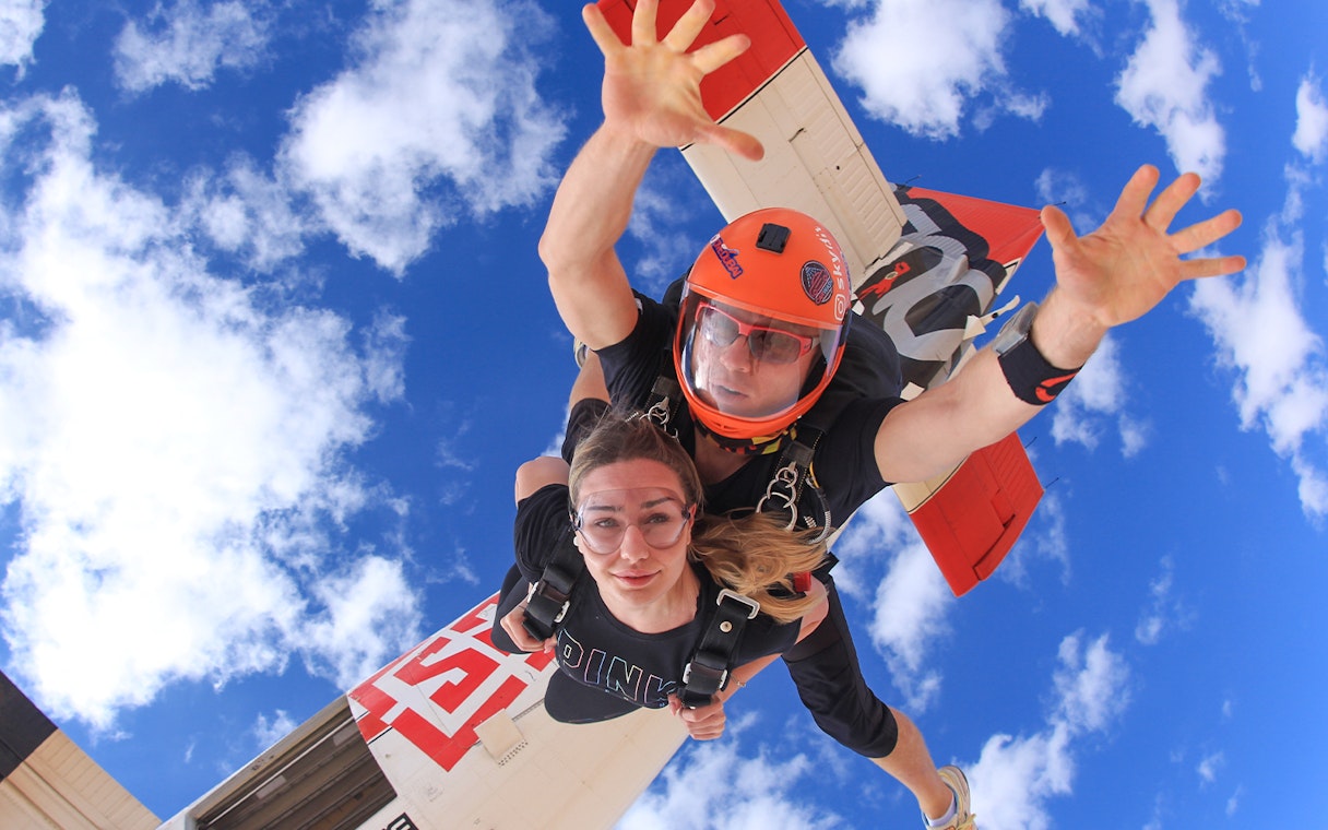 Tandem skydiving over Dubai desert with clear blue sky.