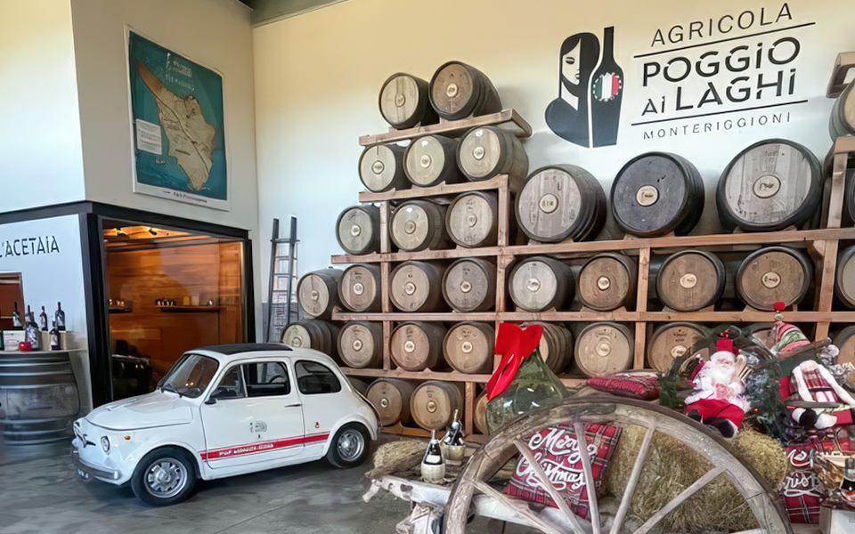 Wine barrels stacked in a Chianti winery, Monteriggioni, Italy, with a vintage car display.