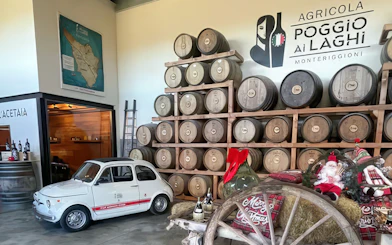 Wine barrels stacked in a Chianti winery, Monteriggioni, Italy, with a vintage car display.