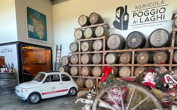 Wine barrels stacked in a Chianti winery, Monteriggioni, Italy, with a vintage car display.