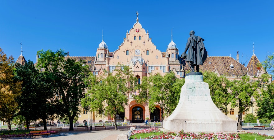 Town hall in Kecskemét, Hungary with a statue in the foreground.