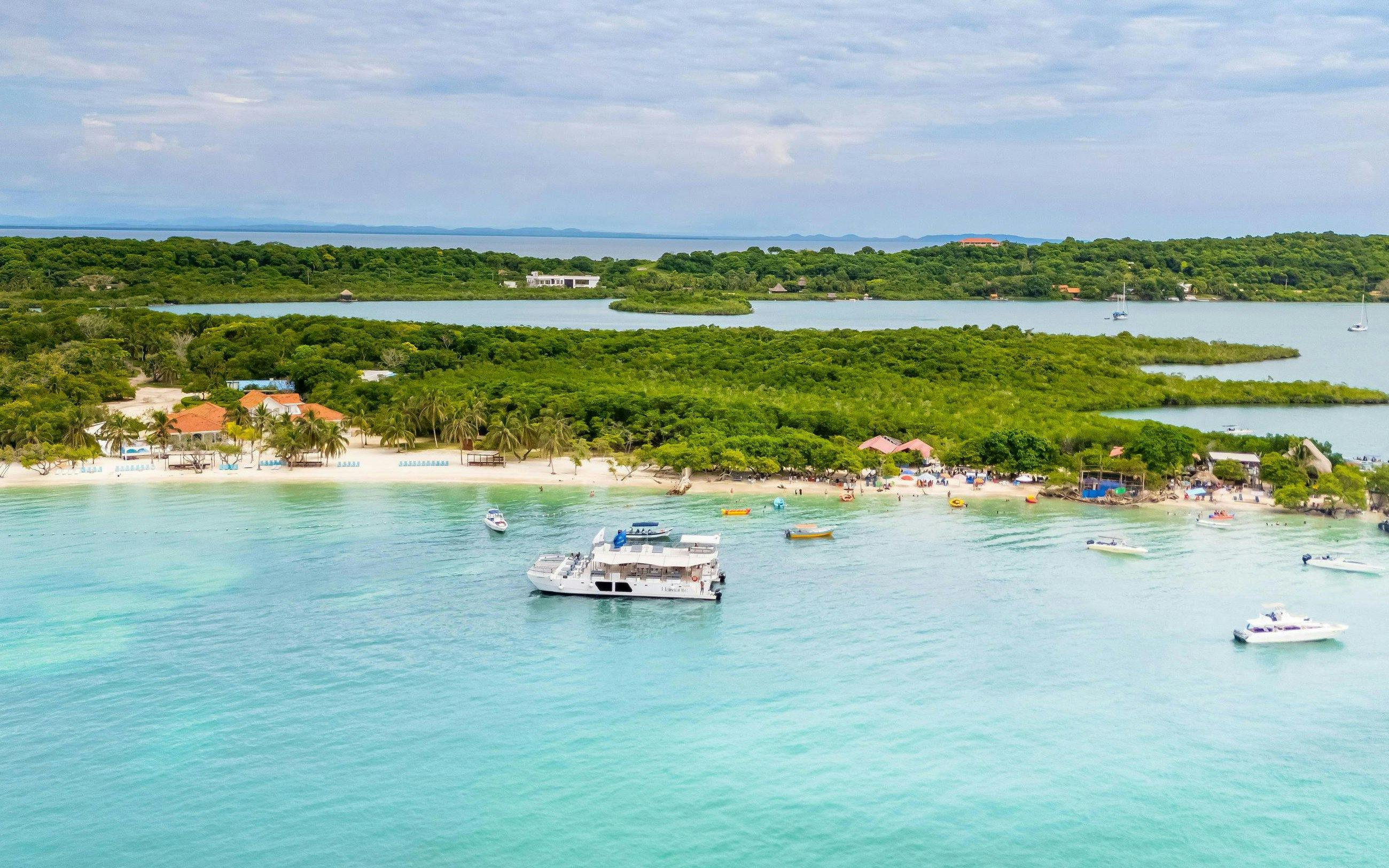 Catamaran anchored near a lush island beach in Cartagena, with small boats and clear blue water.