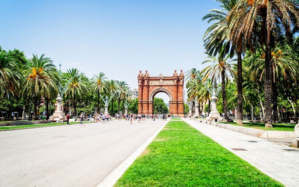 Arc de Triomf in Barcelona with palm trees and tourists walking nearby.