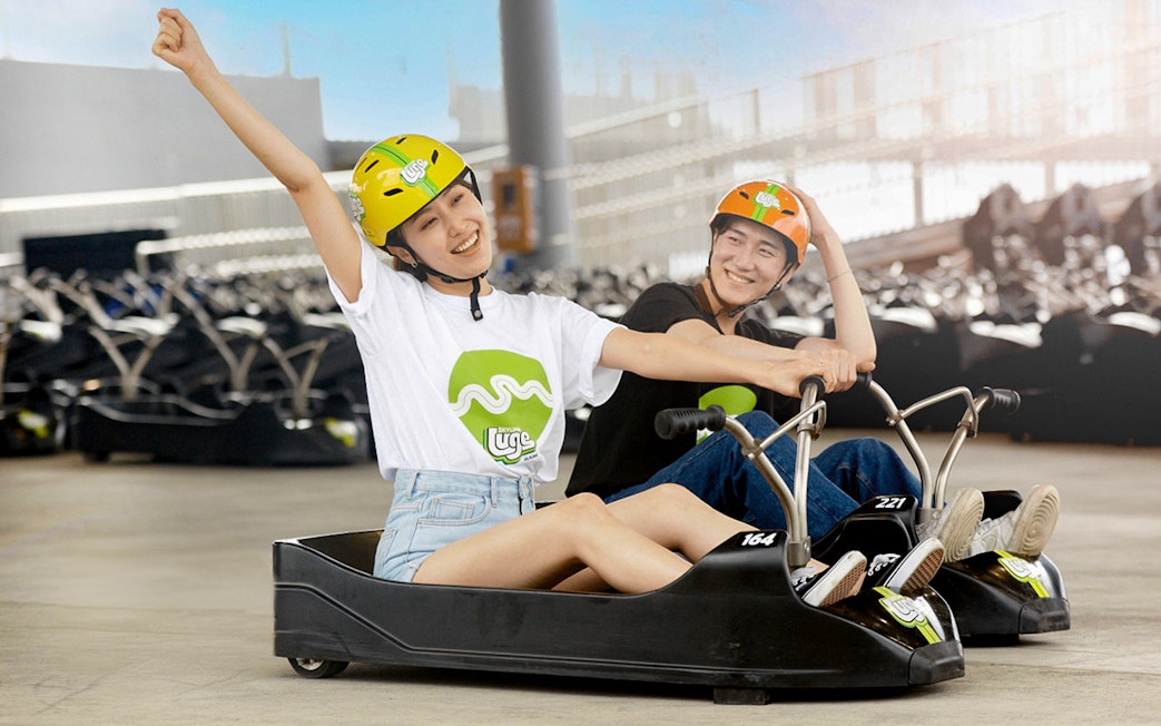 Two people enjoying a ride at Skyline Luge Busan, wearing helmets and smiling.