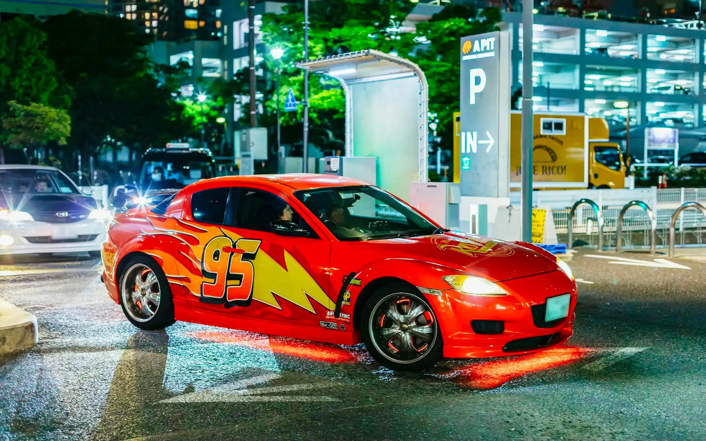 Red sports car with number 95 in Tokyo parking lot at night.