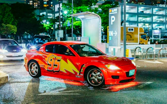 Red sports car with number 95 in Tokyo parking lot at night.