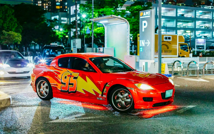Red sports car with number 95 in Tokyo parking lot at night.