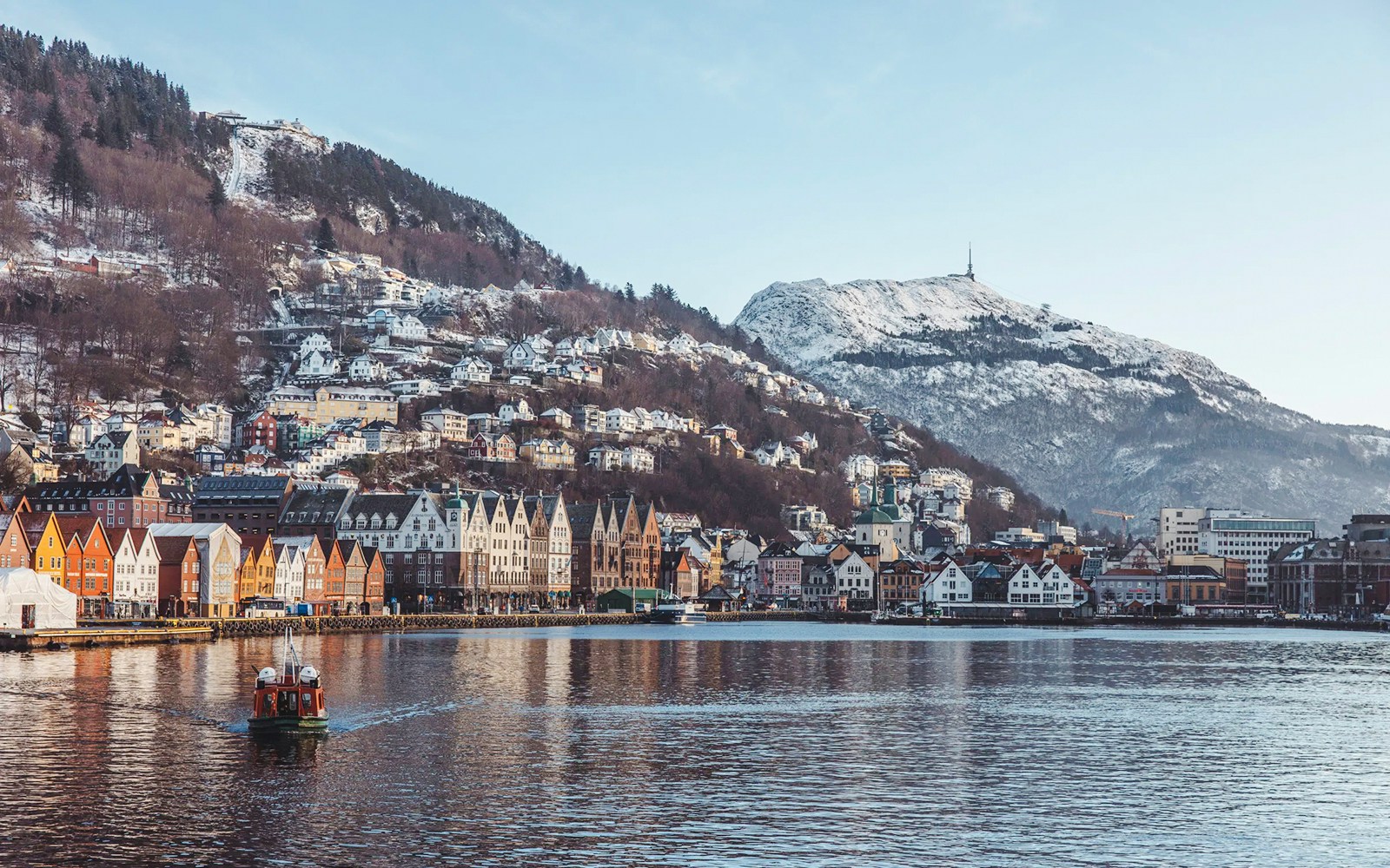 Bryggen harbor with colorful buildings and snow-covered mountains in Bergen, Norway.