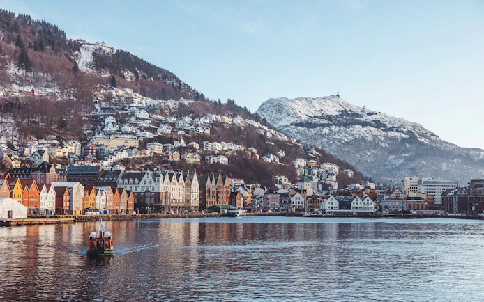 Bryggen harbor with colorful buildings and snow-covered mountains in Bergen, Norway.