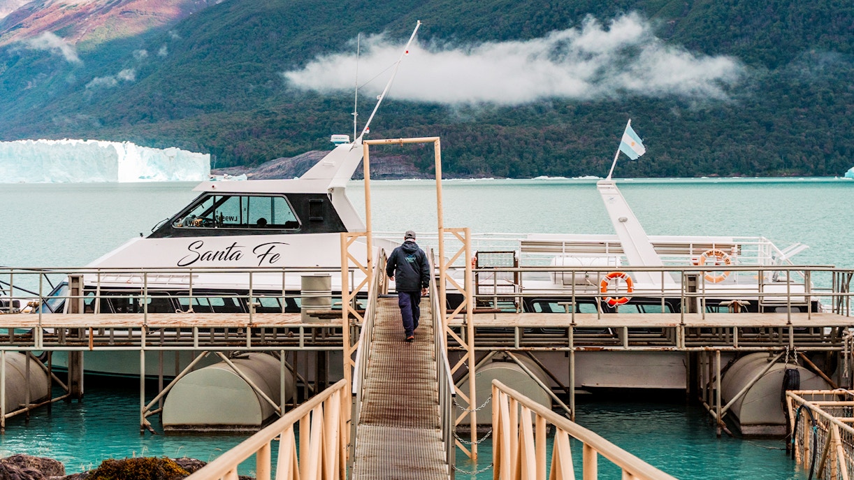 Person walking towards Perito Moreno cruise boarding point with glacier in background.