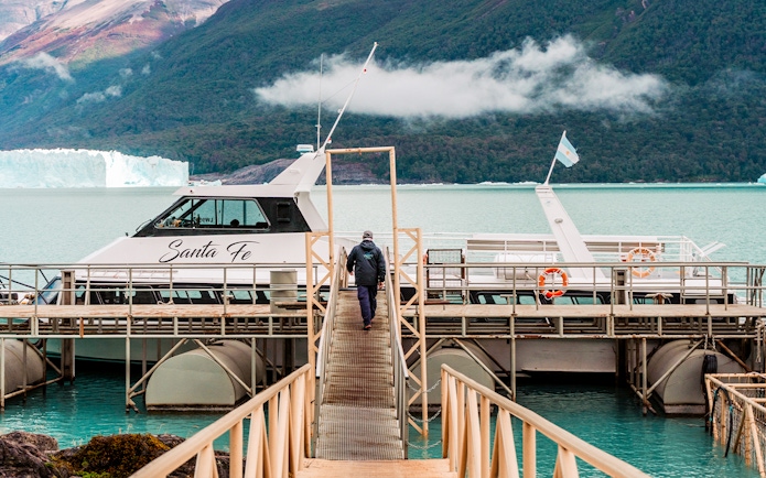 Person walking towards Perito Moreno cruise boarding point with glacier in background.