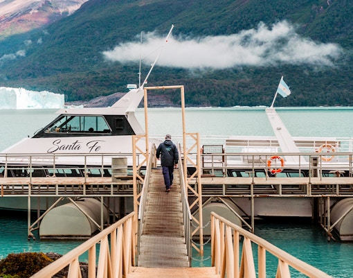 Person walking towards Perito Moreno cruise boarding point with glacier in background.