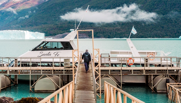 Person walking towards Perito Moreno cruise boarding point with glacier in background.