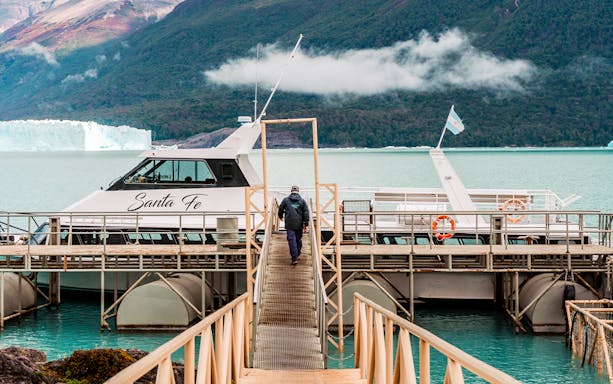 Person walking towards Perito Moreno cruise boarding point with glacier in background.