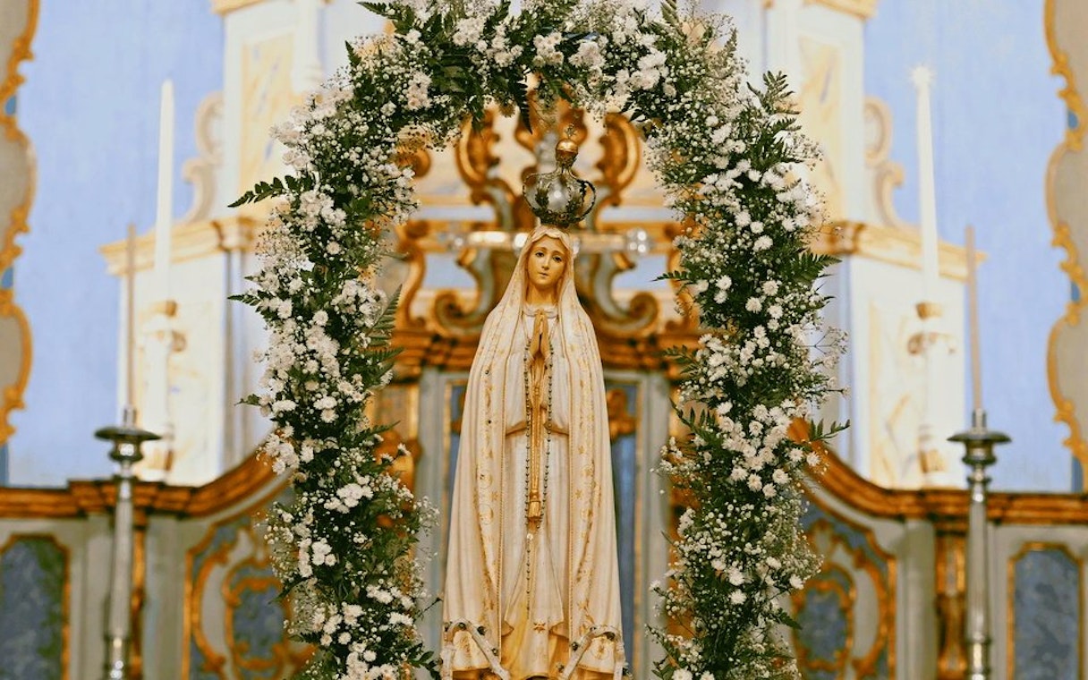 Statue of Our Lady of Fatima adorned with flowers in a church setting.